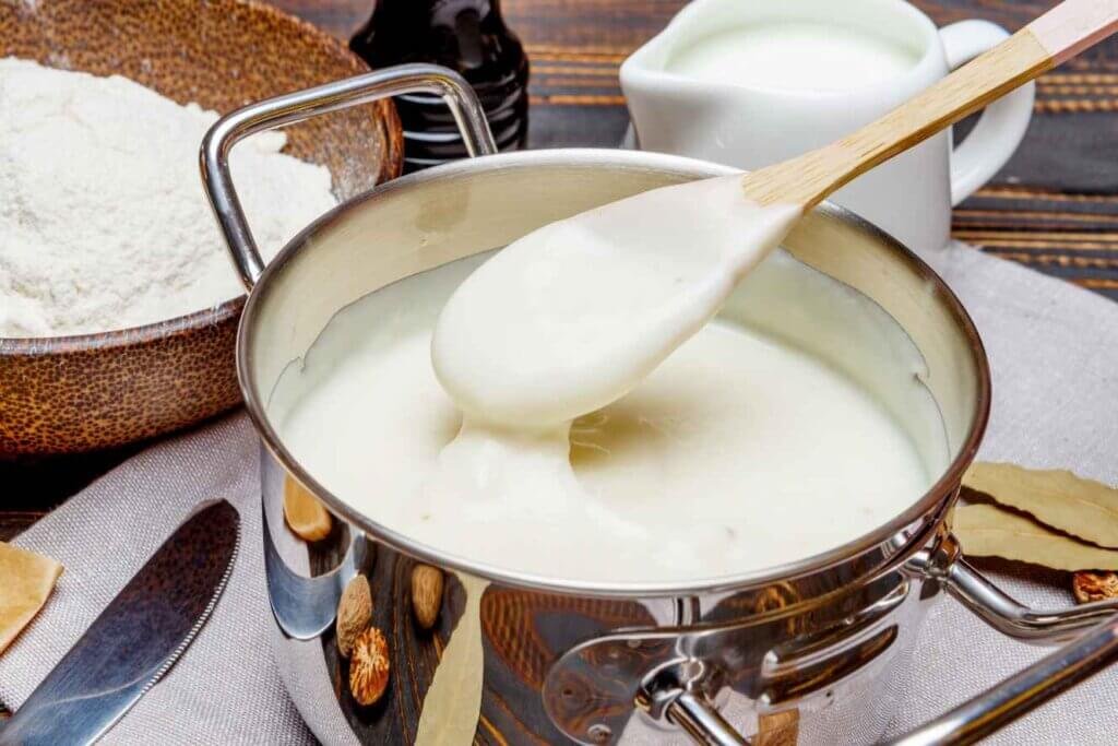 Thick homemade béchamel sauce coating a wooden spoon above a saucepan.