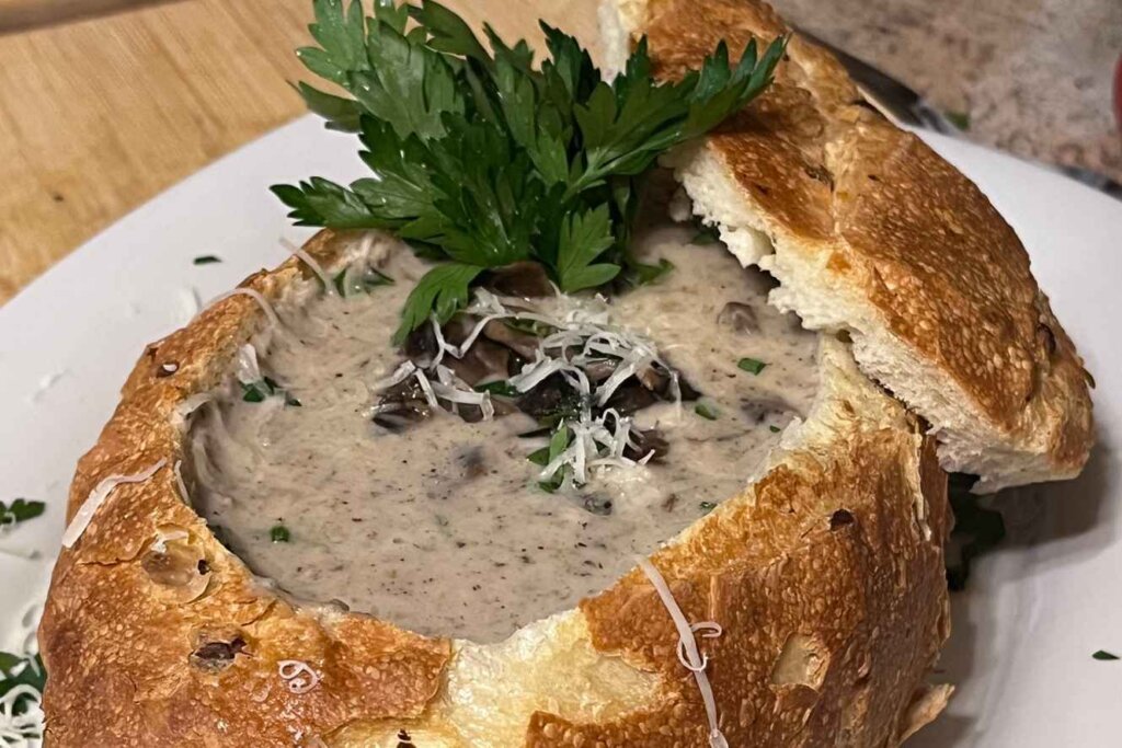Creamy mushroom soup served in a toasted bread bowl with Parmesan cheese and fresh parsley.