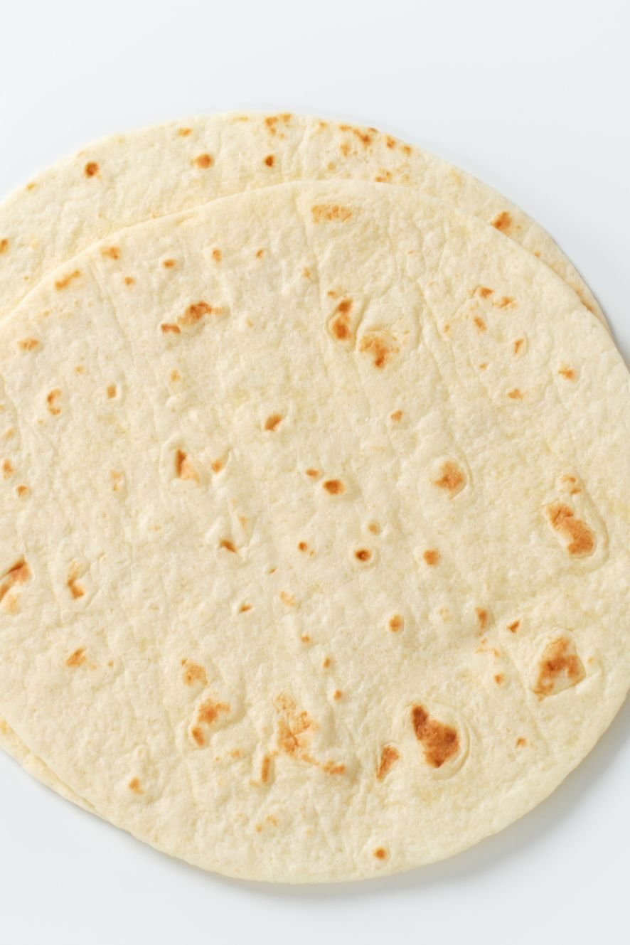 Soft homemade flour tortillas with lightly browned spots stacked on a white surface.