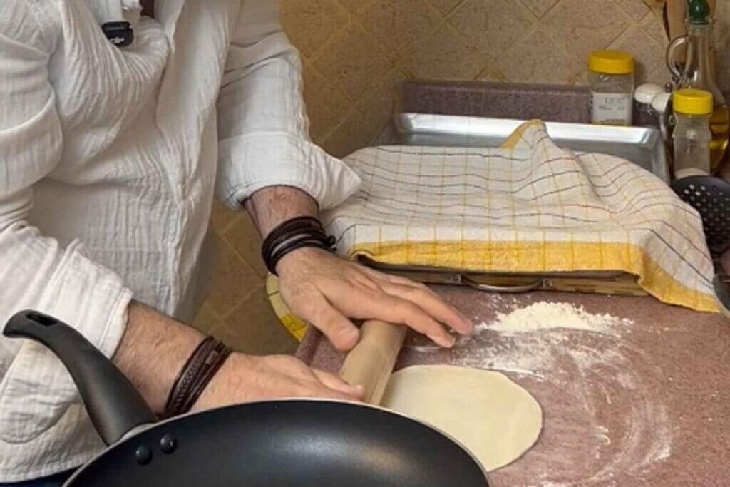 Chef rolling a portion of flour tortillas dough into a thin circle beside a frying pan.