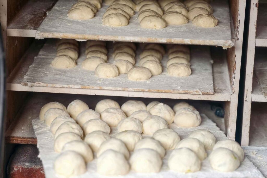 Portioned flour tortilla dough balls resting on floured trays inside a bakery rack.