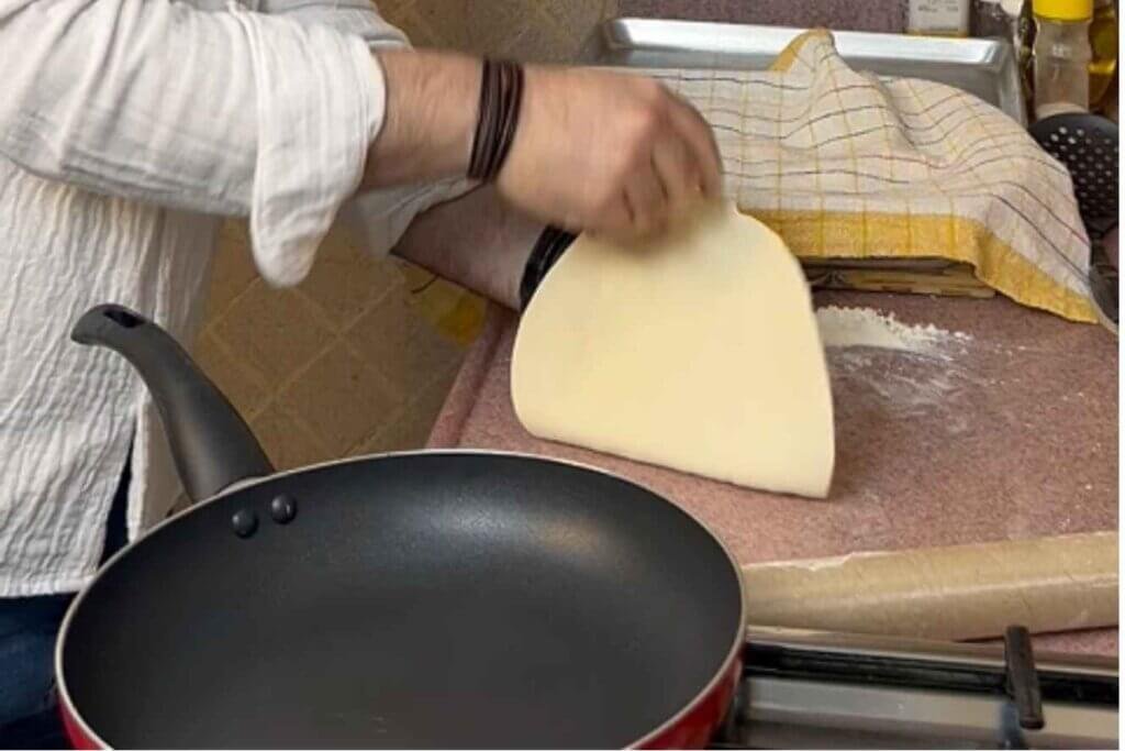 Chef lifting a thinly rolled flour tortilla before placing it in a hot frying pan.