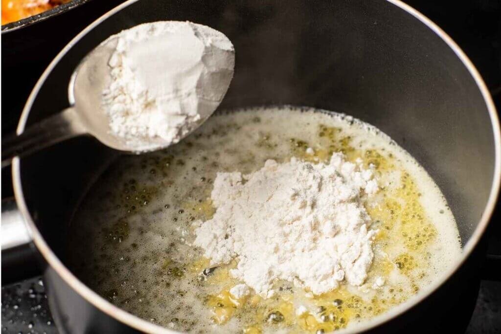 Flour being added to melted butter to make a roux for homemade béchamel sauce.