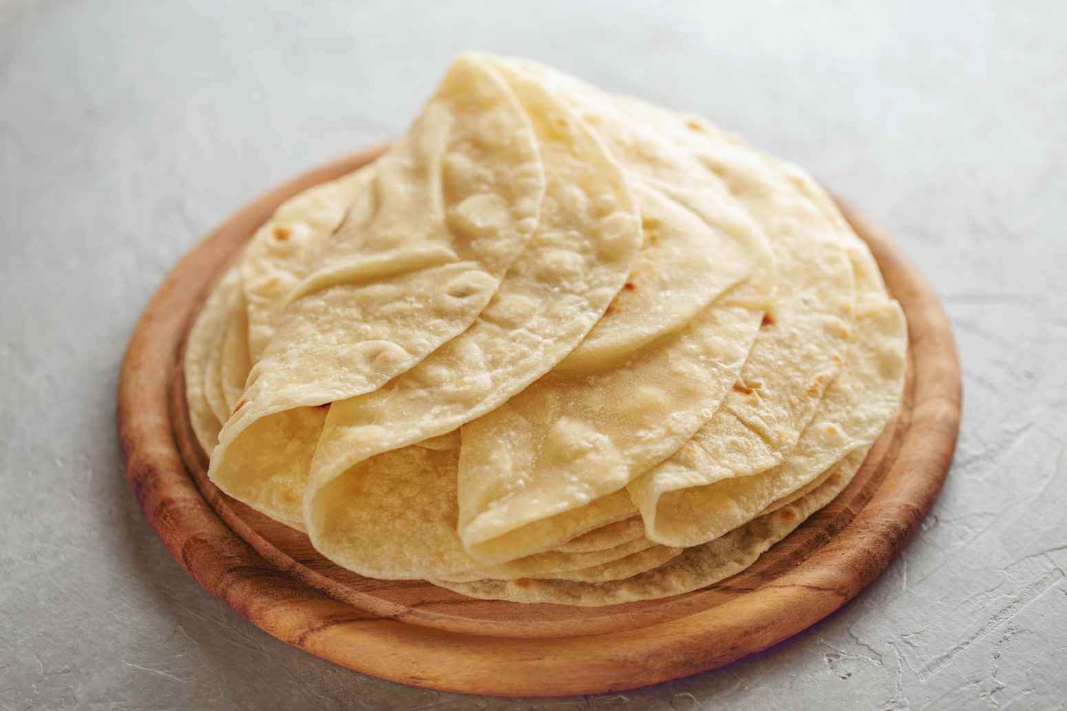 Soft homemade flour tortillas folded and stacked on a round wooden serving board.