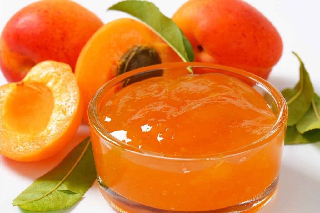 Smooth apricot jam in a glass bowl surrounded by fresh apricots