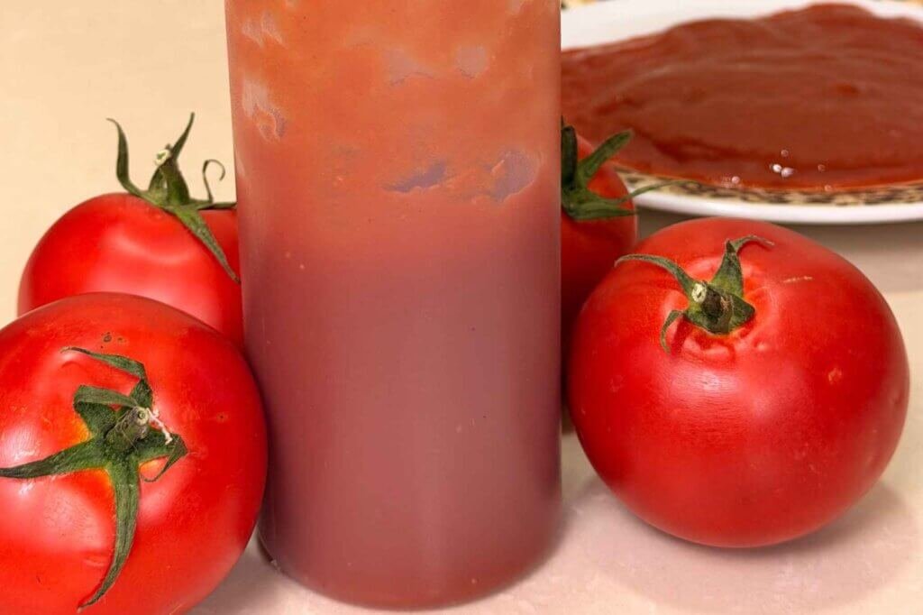 Bottle of homemade ketchup surrounded by fresh red tomatoes