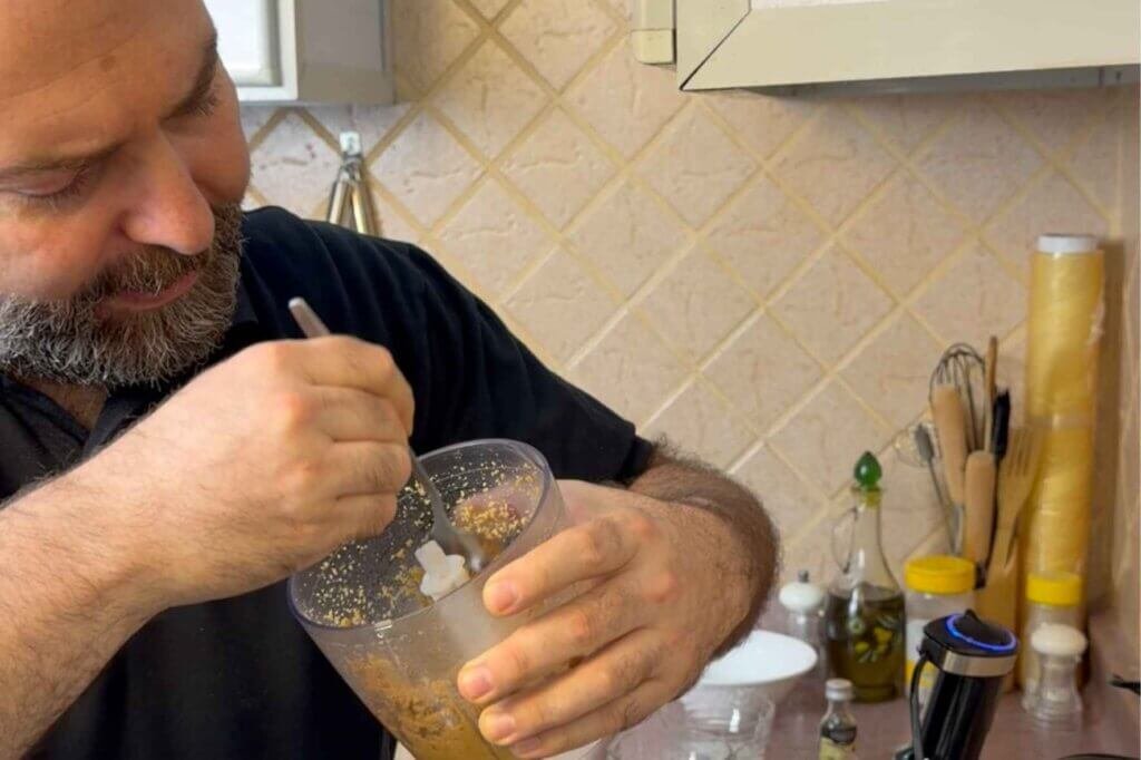 Chef François tastes a hazelnut mixture from a food processor bowl while preparing homemade chocolate spread.