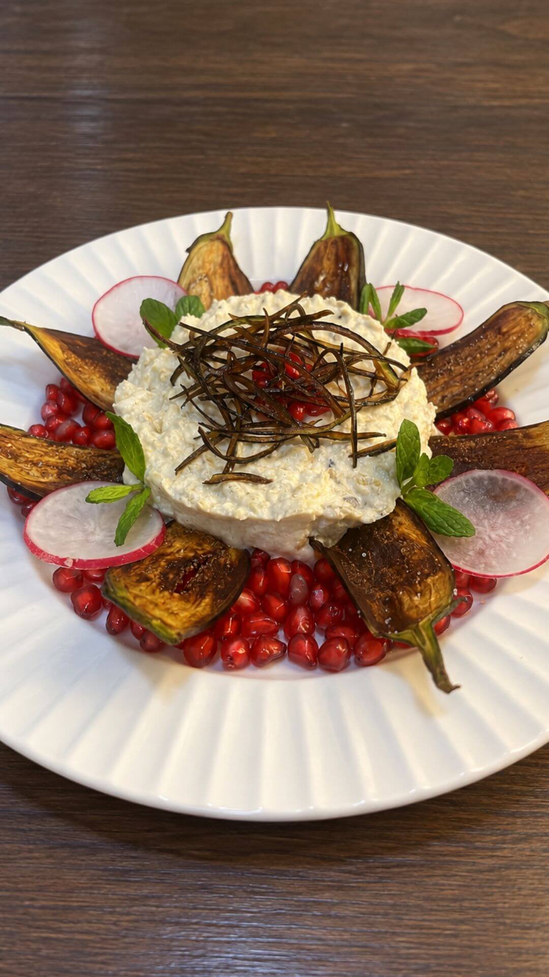 Lebanese eggplant mtabbal topped with crispy eggplant strips and surrounded by roasted eggplant, pomegranate seeds, radish slices, and fresh mint.