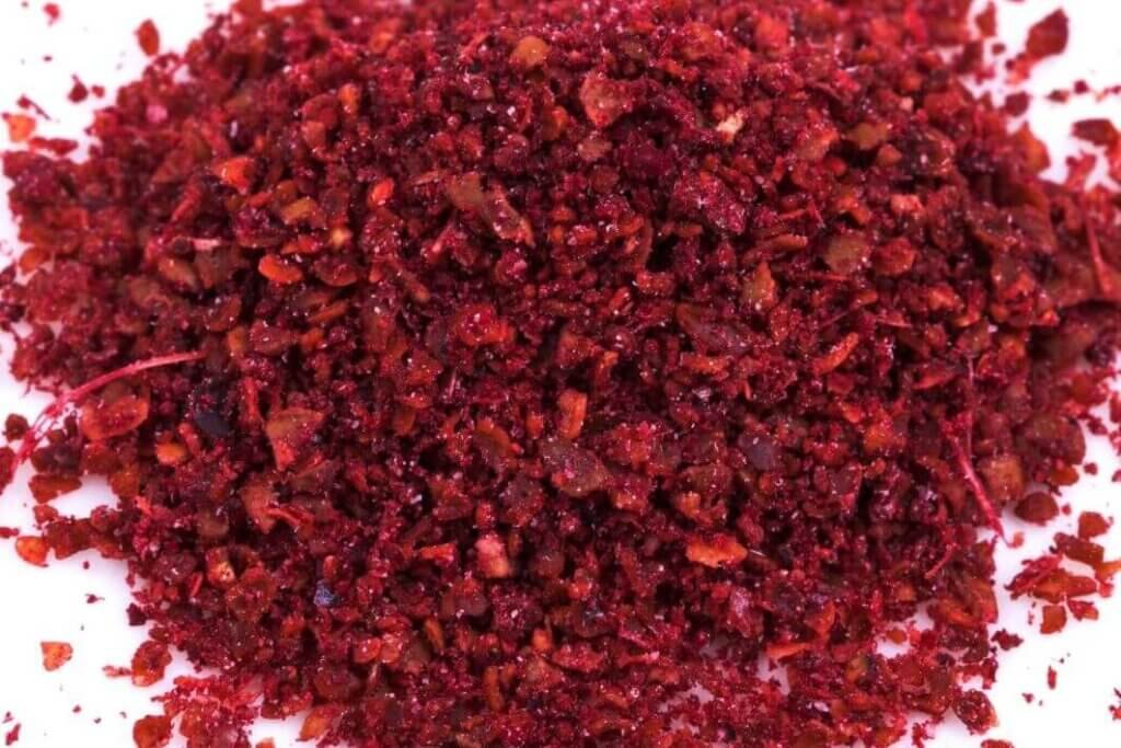 Close-up of freshly ground dark red sumac spice with a coarse texture on a white background.