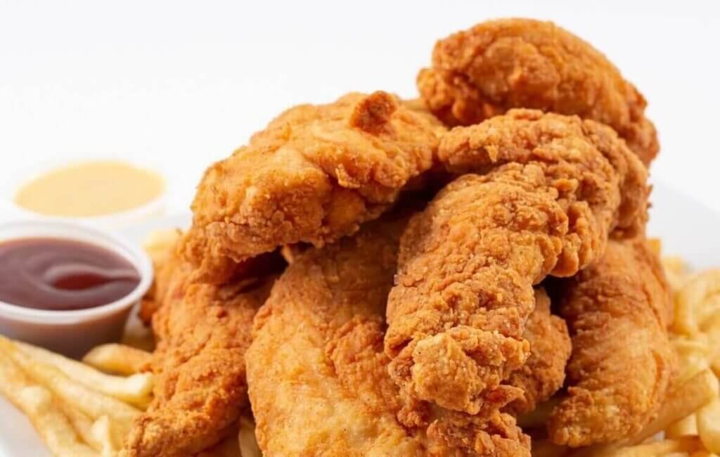 Golden crispy fish sticks served on a white plate with French fries and dipping sauces, showcasing a crunchy coating and tender fish inside.
