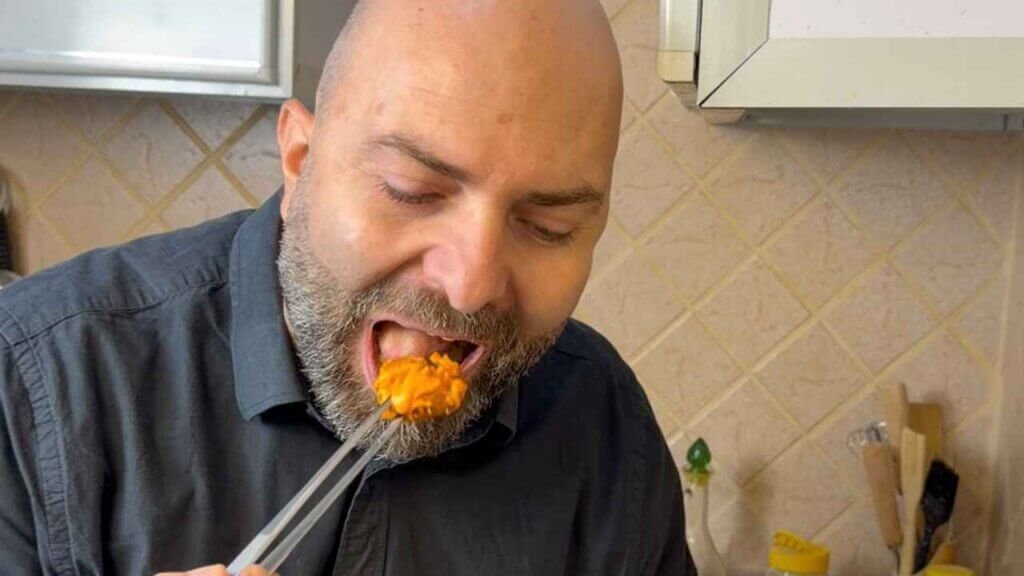 Chef François El Aaraj tasting a dynamite shrimp coated in orange sauce, using chopsticks in his kitchen.