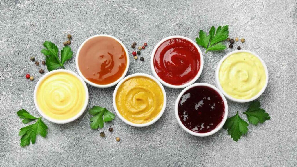 Six bowls of colorful dipping sauces on a gray surface with parsley and peppercorns, illustrating pairing ideas for dynamite sauce.