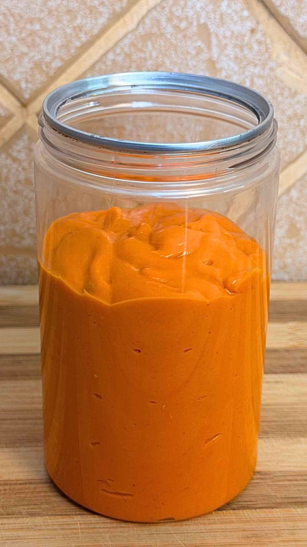 Thick orange dynamite sauce in an open glass jar on a wooden countertop.