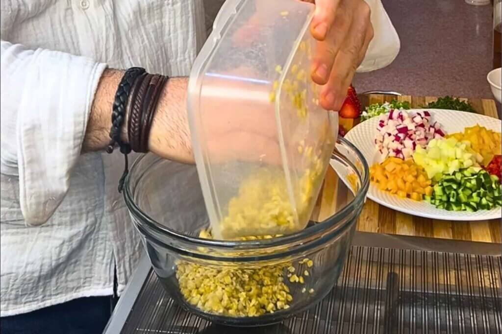 Chef François pouring cooked smoked freekeh into a clear glass mixing bowl, with freshly chopped fruits and vegetables ready for the salad.